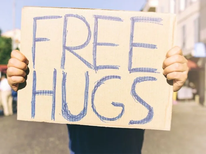 Người đàn ông với bảng "Free Hugs" và một người phụ nữ đang ôm anh ấy.