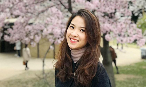 Nguyễn Thị Sao Ly đứng bên cạnh một quyển sách hoặc tạp chí, có thể liên quan đến xuất bản hoặc thành tựu học thuật của cô