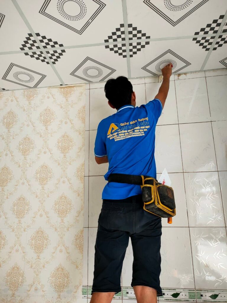 Người thợ đang miết giấy dán tường lên bề mặt gạch men để đảm bảo độ bám dính